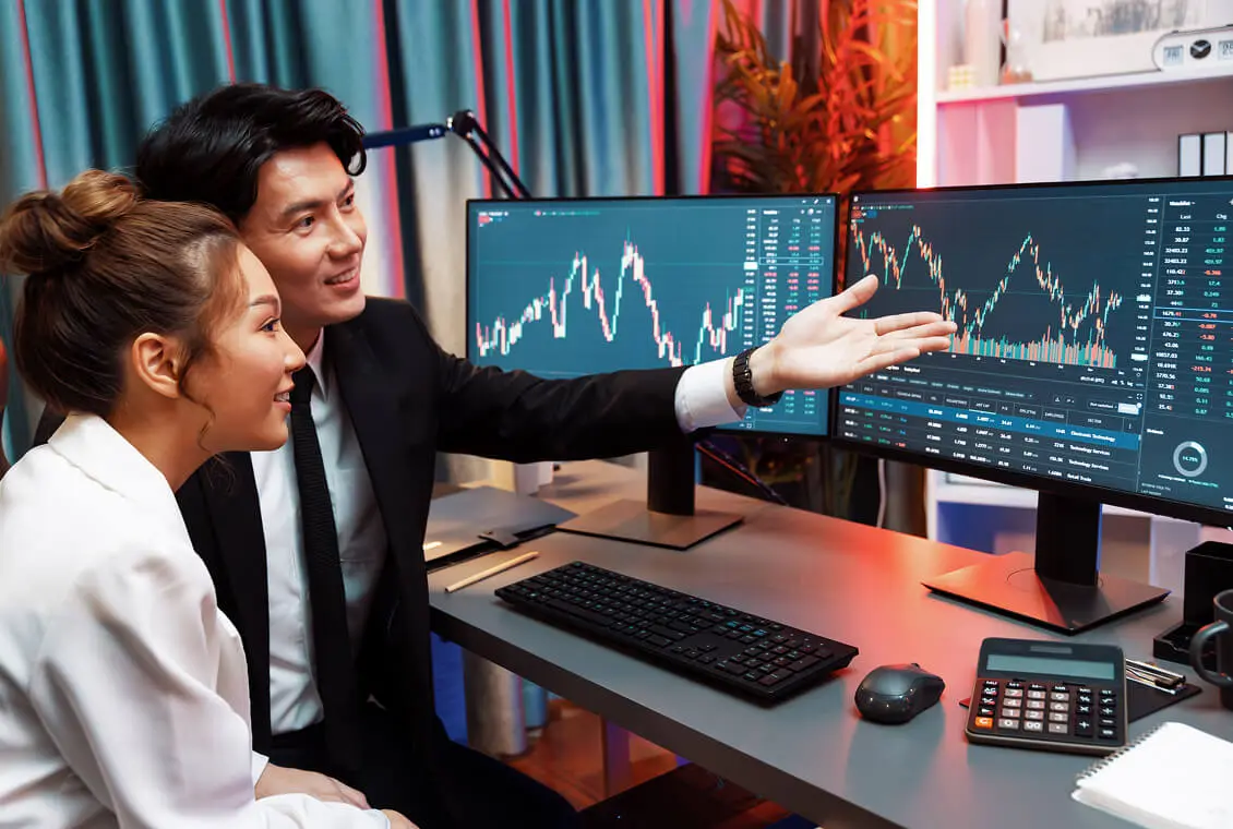 Business professionals reviewing stock market charts on dual monitors